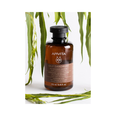 Frasco âmbar de shampoo Apivita OILY DANDRUFF com tampa preta e folhas verdes ao redor