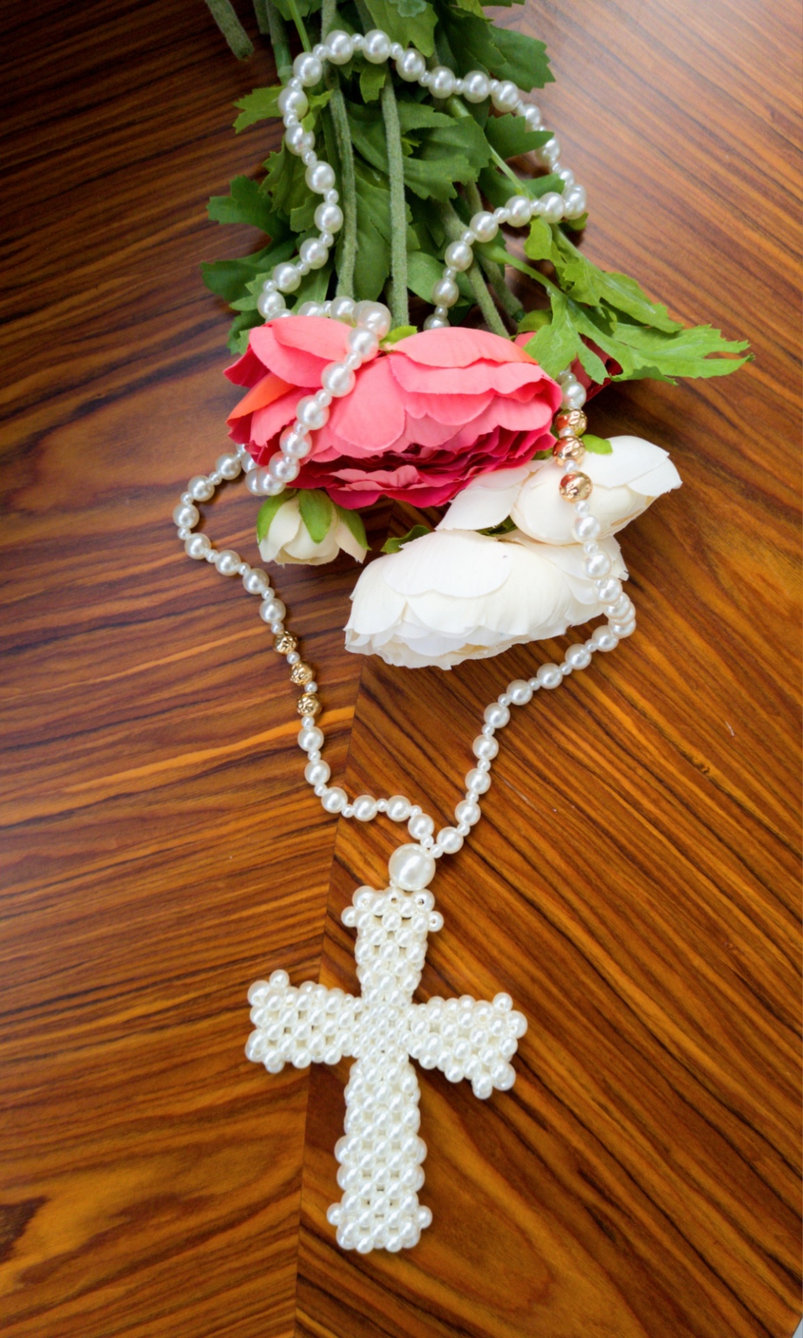 Colar de pérolas com crucifixo em forma de cruz e flores artificiais sobre mesa de madeira
