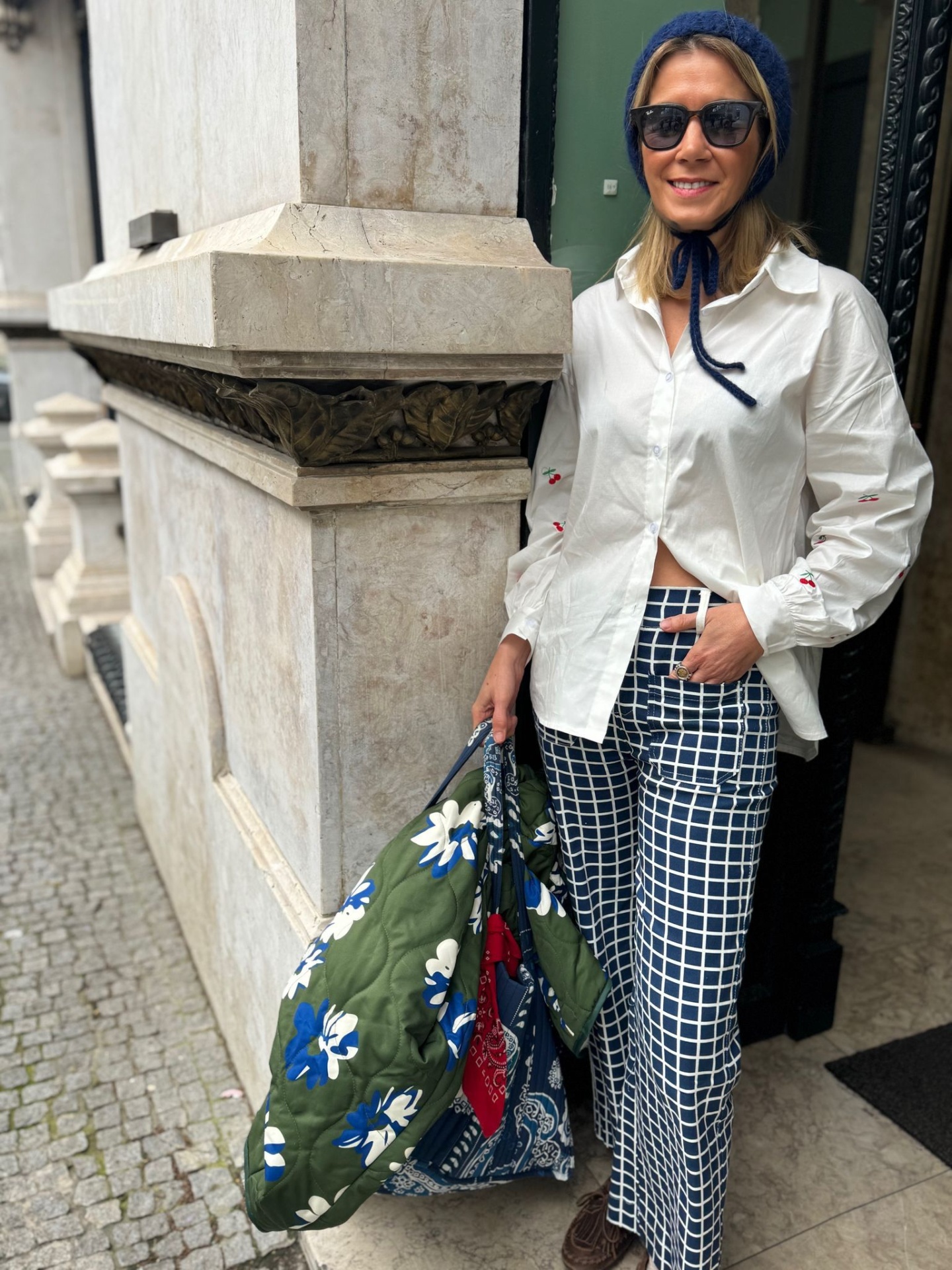 Mulher com roupa casual e bolsa acolchoada floral numa rua com calçada de pedra.