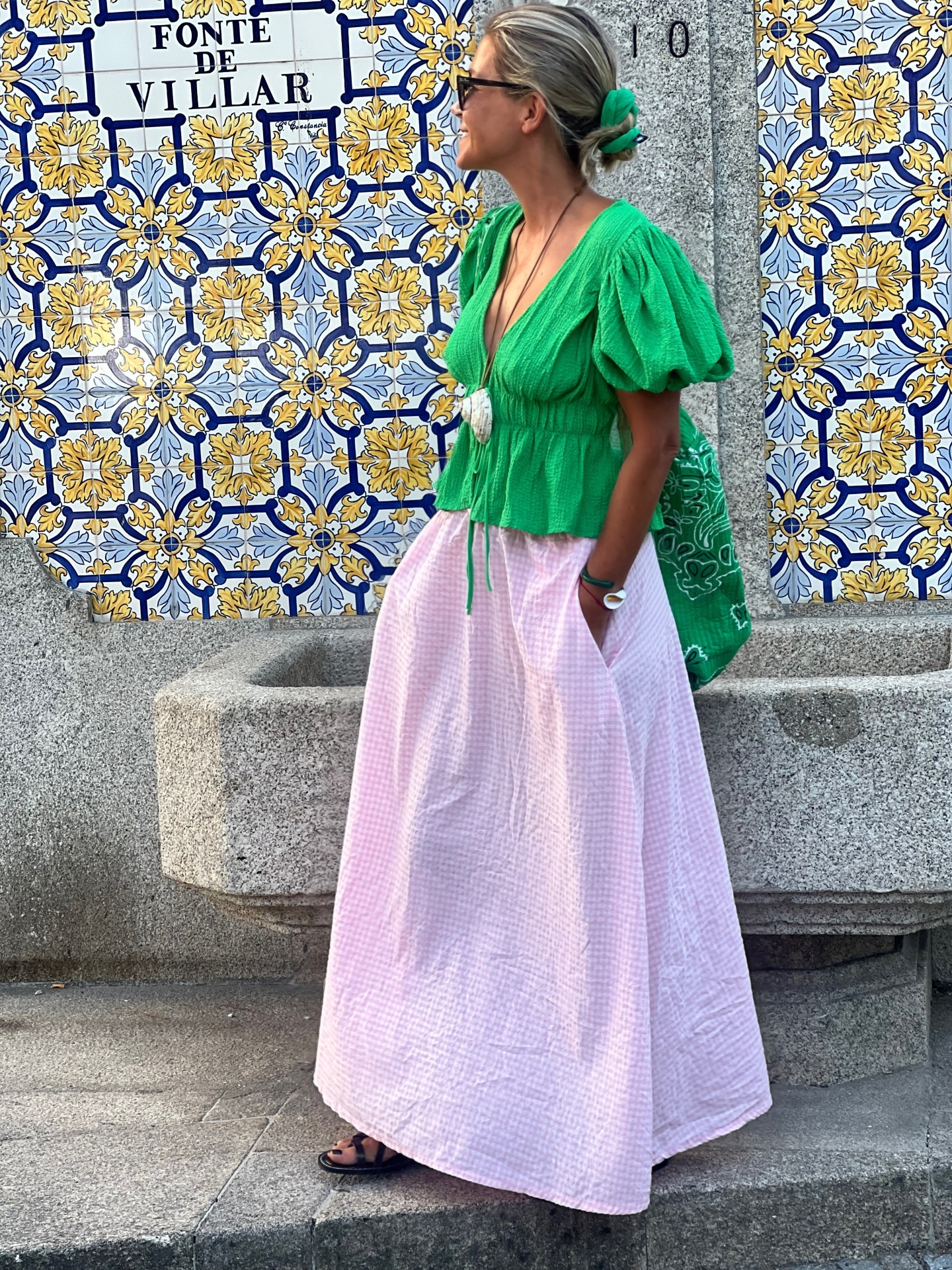 Mulher de roupa verde e rosa ao lado de azulejos azuis e amarelos com texto Fonte de Villar