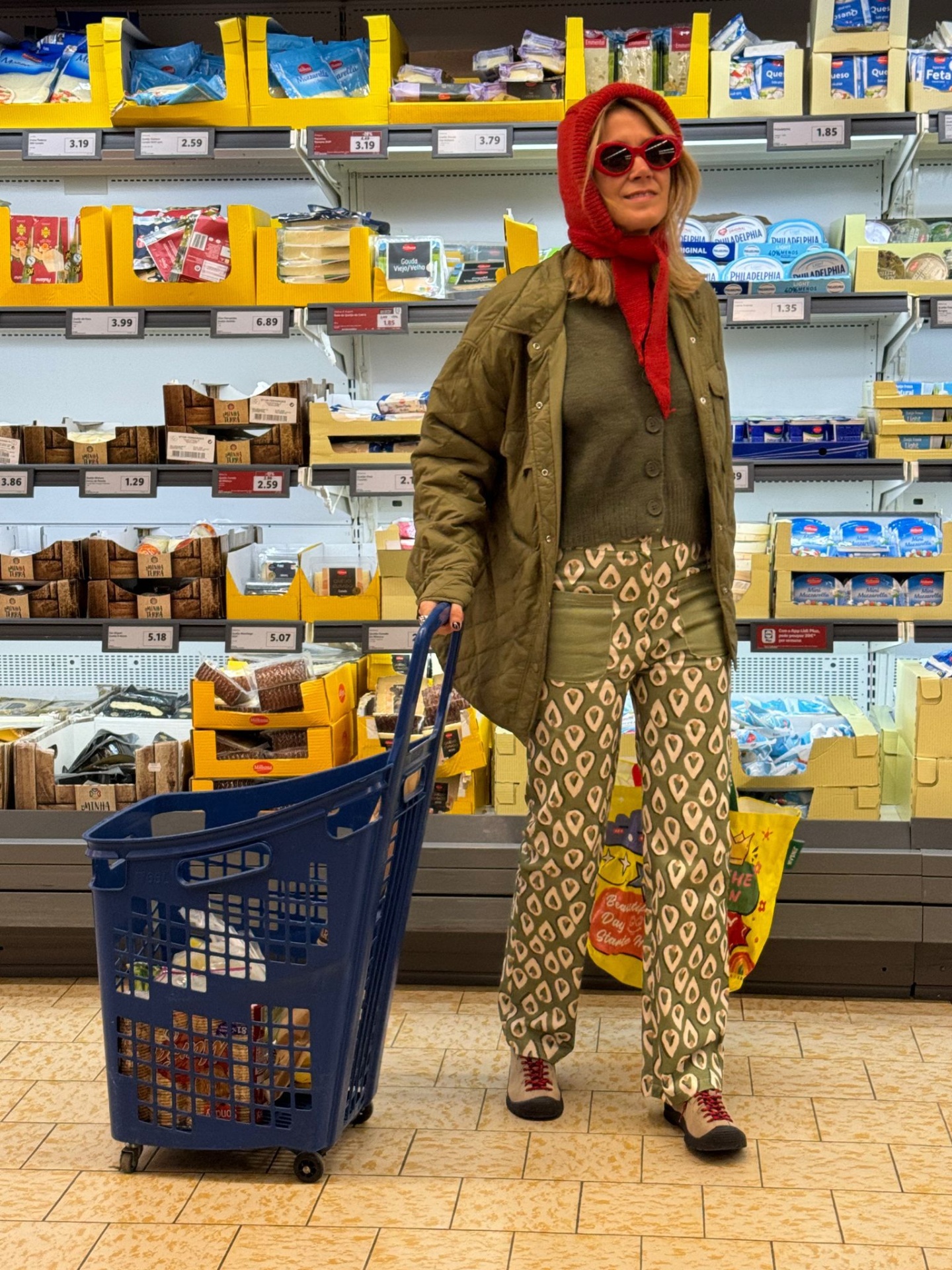 Mulher com roupa colorida a empurrar carrinho vazio num supermercado com prateleiras ao fundo