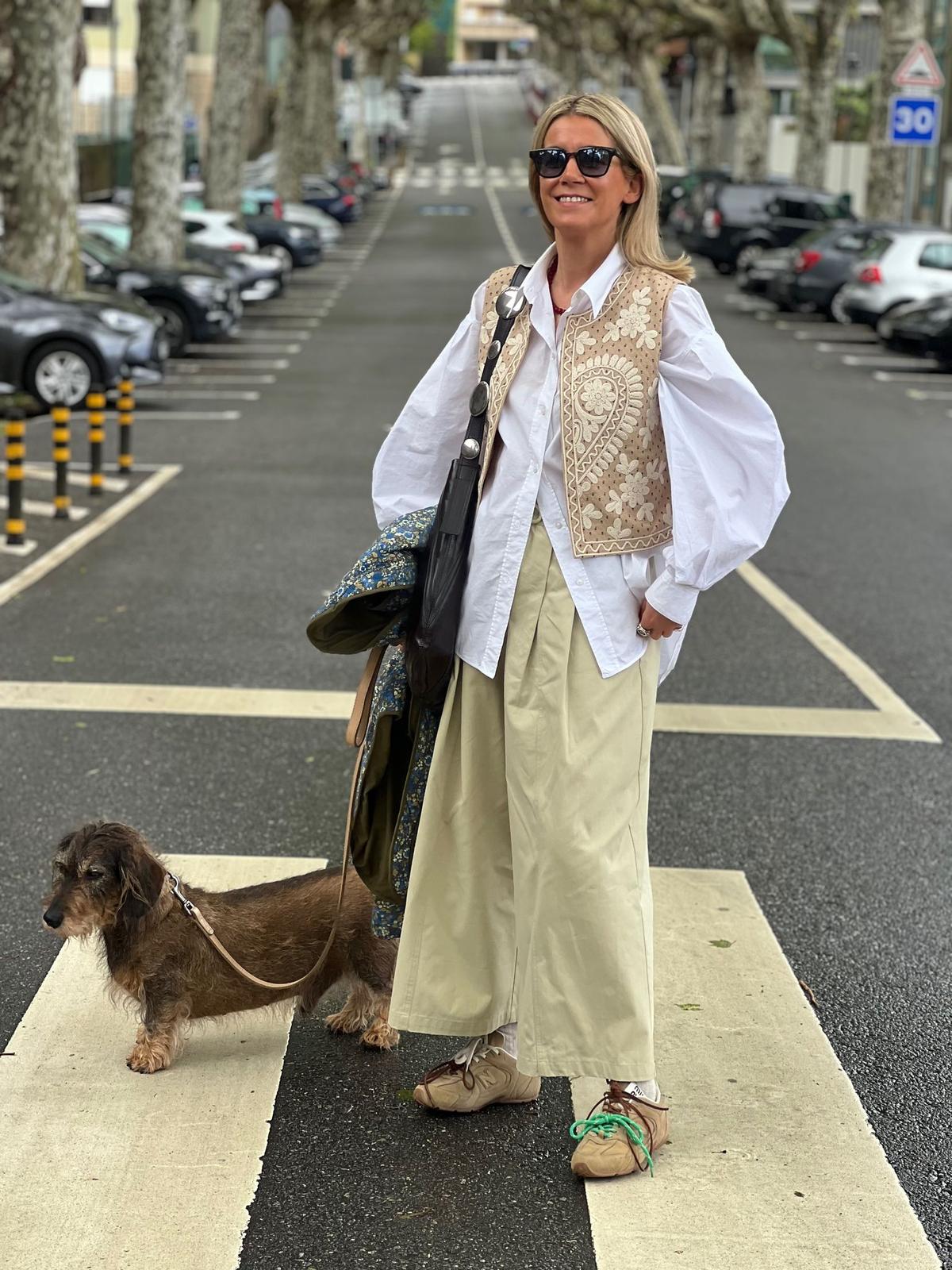Mulher com roupa clara e colete bege com cão numa passadeira na rua