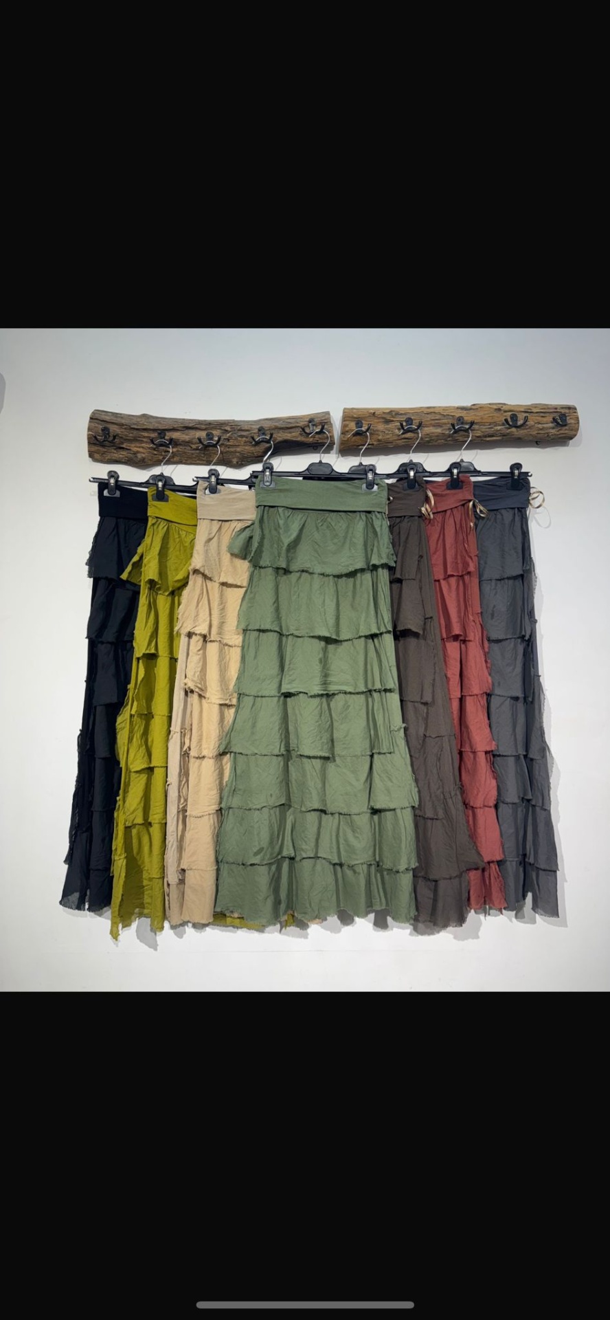 Seis saias compridas com pregas de várias cores penduradas numa régua de madeira