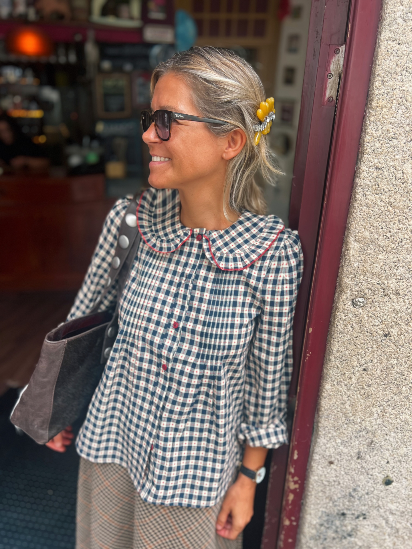 Blusa quadriculada azul e creme com botões vermelhos e gola arredondada, mola de cabelo amarela, mulher com óculos de sol pretos