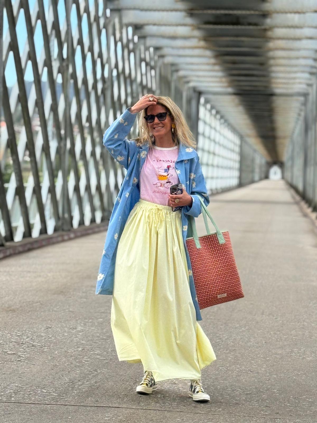Mulher com casaco azul, saia amarela e t-shirt rosa em passadeira metálica