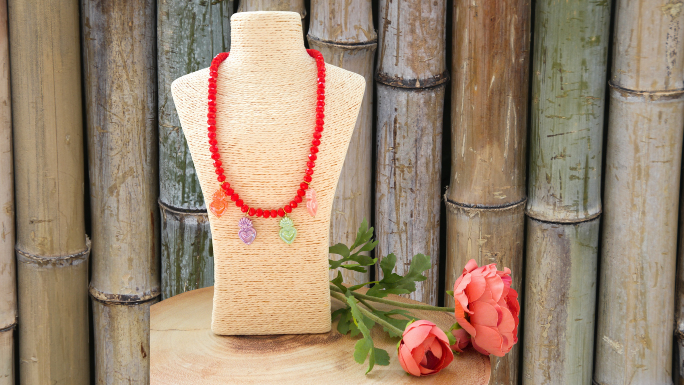 Colar vermelho com pendentes de coruja em busto creme com flores cor de rosa e bambus ao fundo