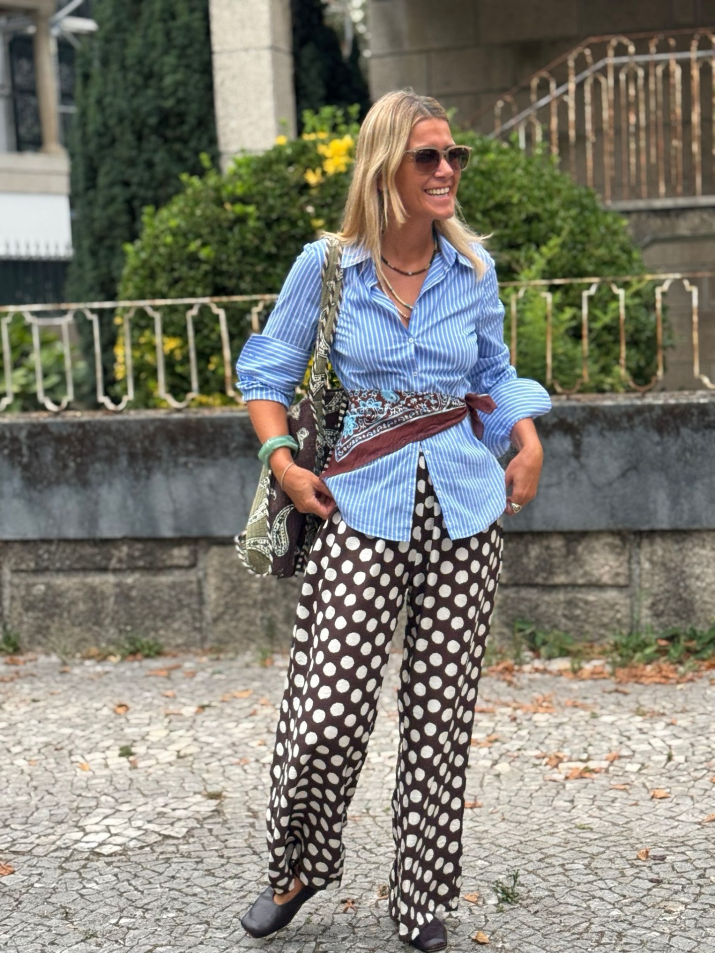 Mulher com camisa azul riscada e calças pretas de bolinhas brancas ao ar livre