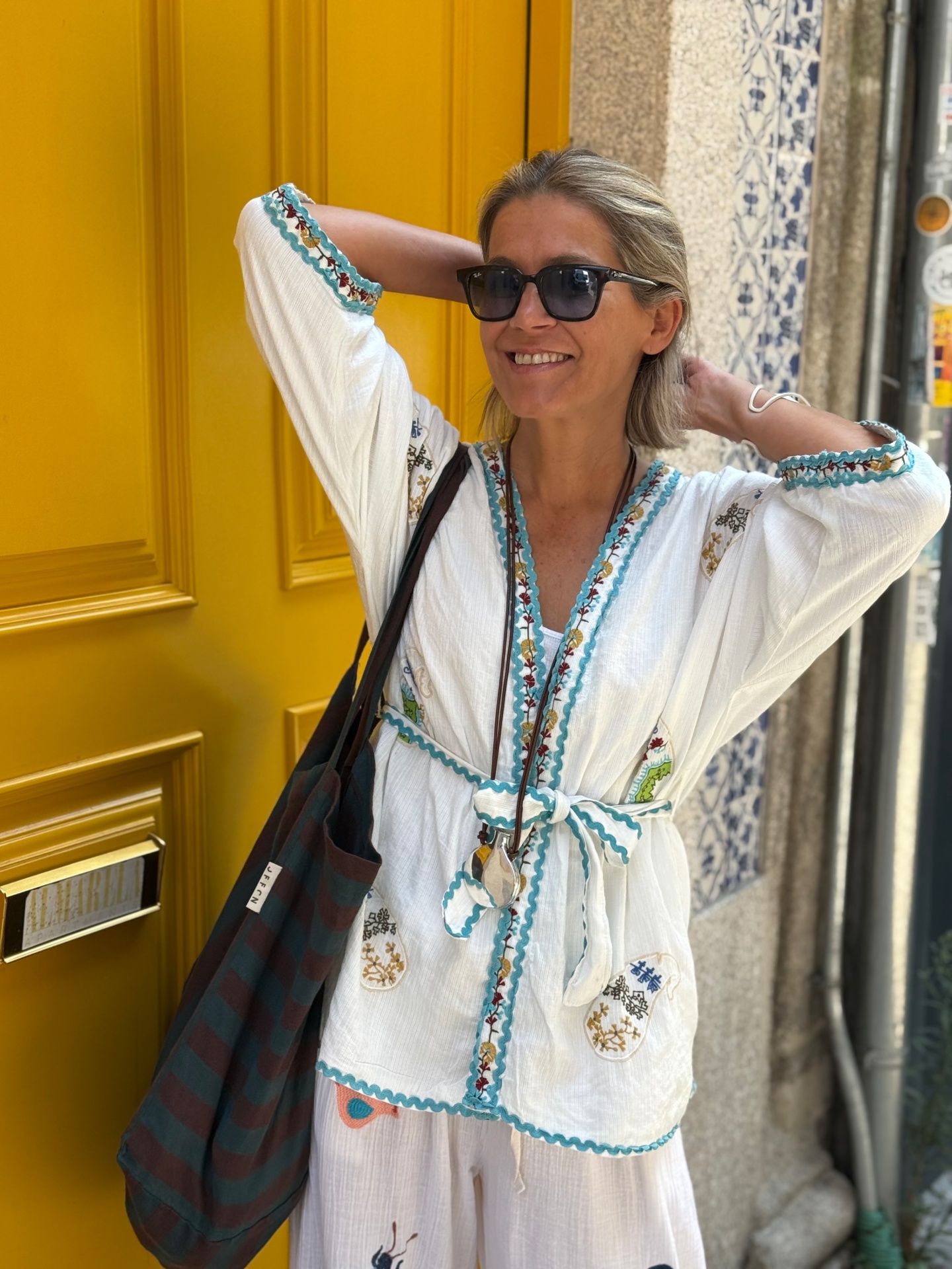 Mulher com blusa branca bordada, calças brancas e óculos de sol pretos