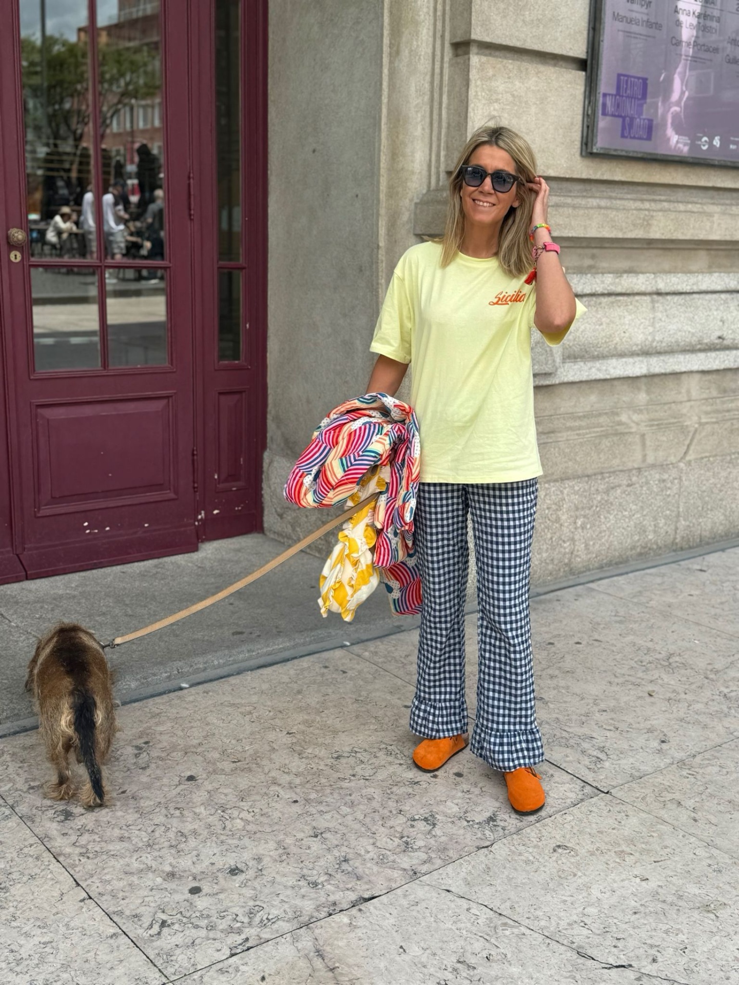 Mulher com roupa colorida e óculos escuros a passear um cão junto a uma porta vermelha