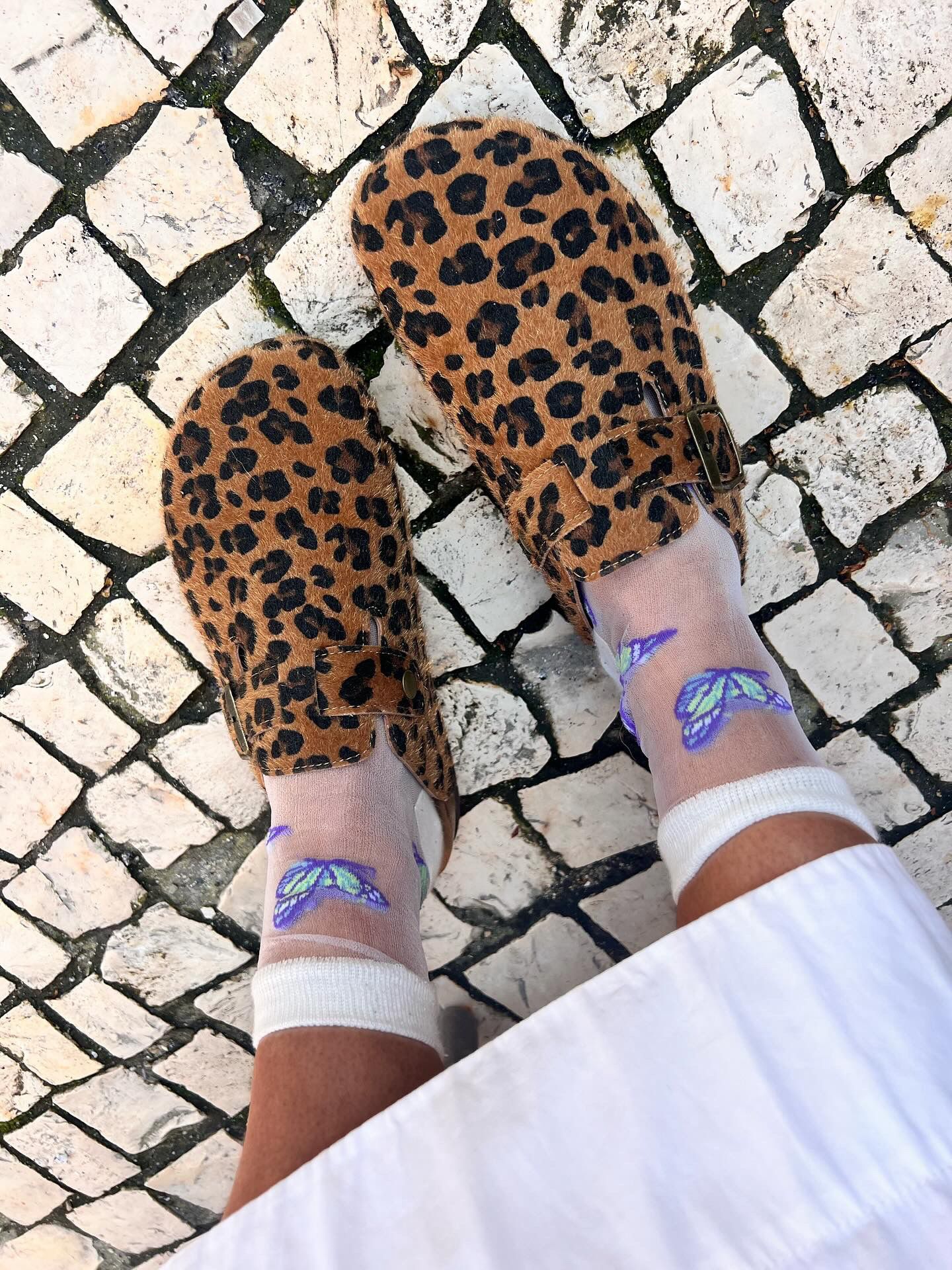 Sapatos mule animal print castanhos com meias transparentes e borboletas azuis em calçada portuguesa