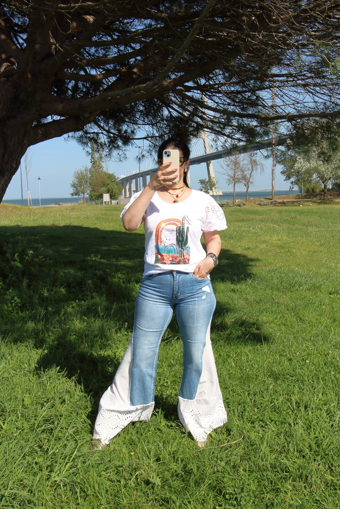 Pessoa com t-shirt branca estampada e calças de ganga com detalhes rendados em branco ao ar livre.