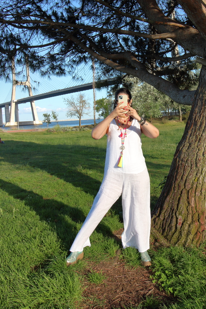 Pessoa de roupa branca a tirar foto com telemóvel junto a árvore e ponte suspensa