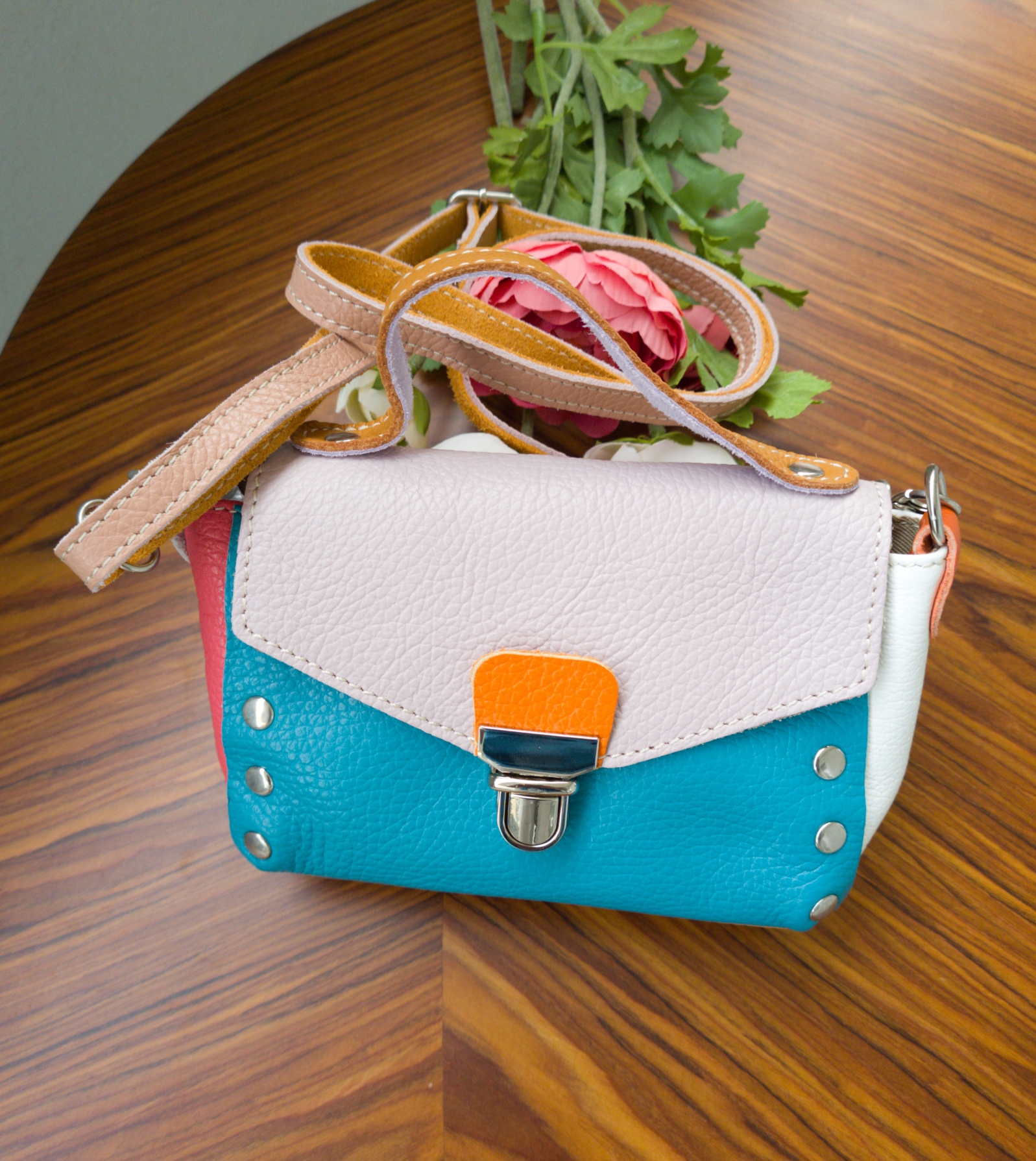 Mala pequena azul turquesa com aba branca e detalhe laranja sobre mesa de madeira