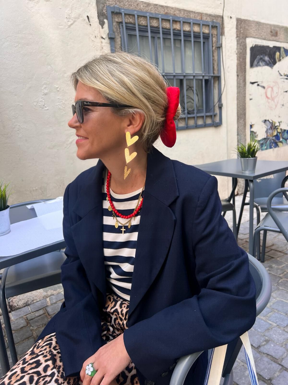Mulher com blazer azul, camisola às riscas, padrão animal print, óculos de sol e acessórios vermelhos e dourados