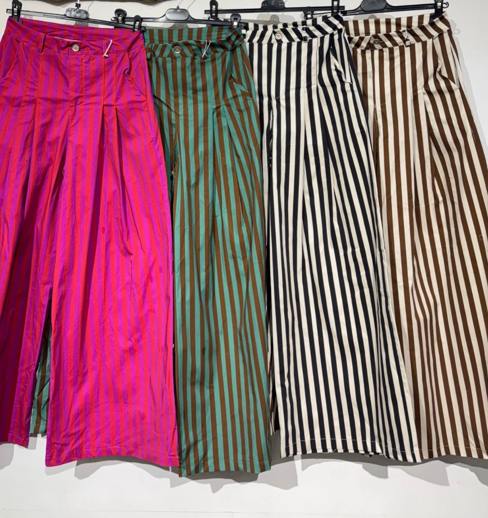 Quatro calças às riscas verticais em várias cores penduradas em cabides.