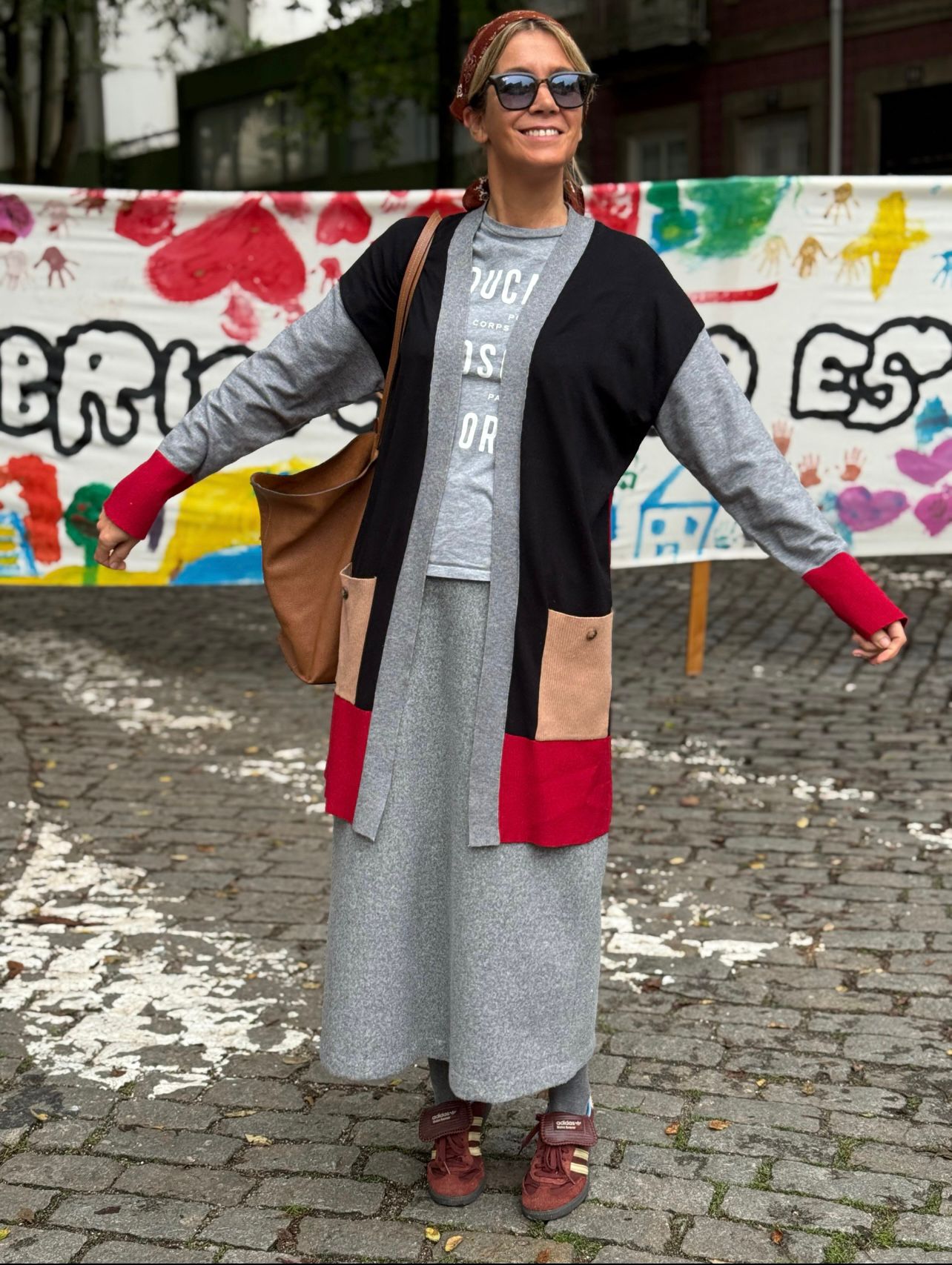 Mulher com cardigan colorido e saia cinza em estrada de pedra com fundo colorido