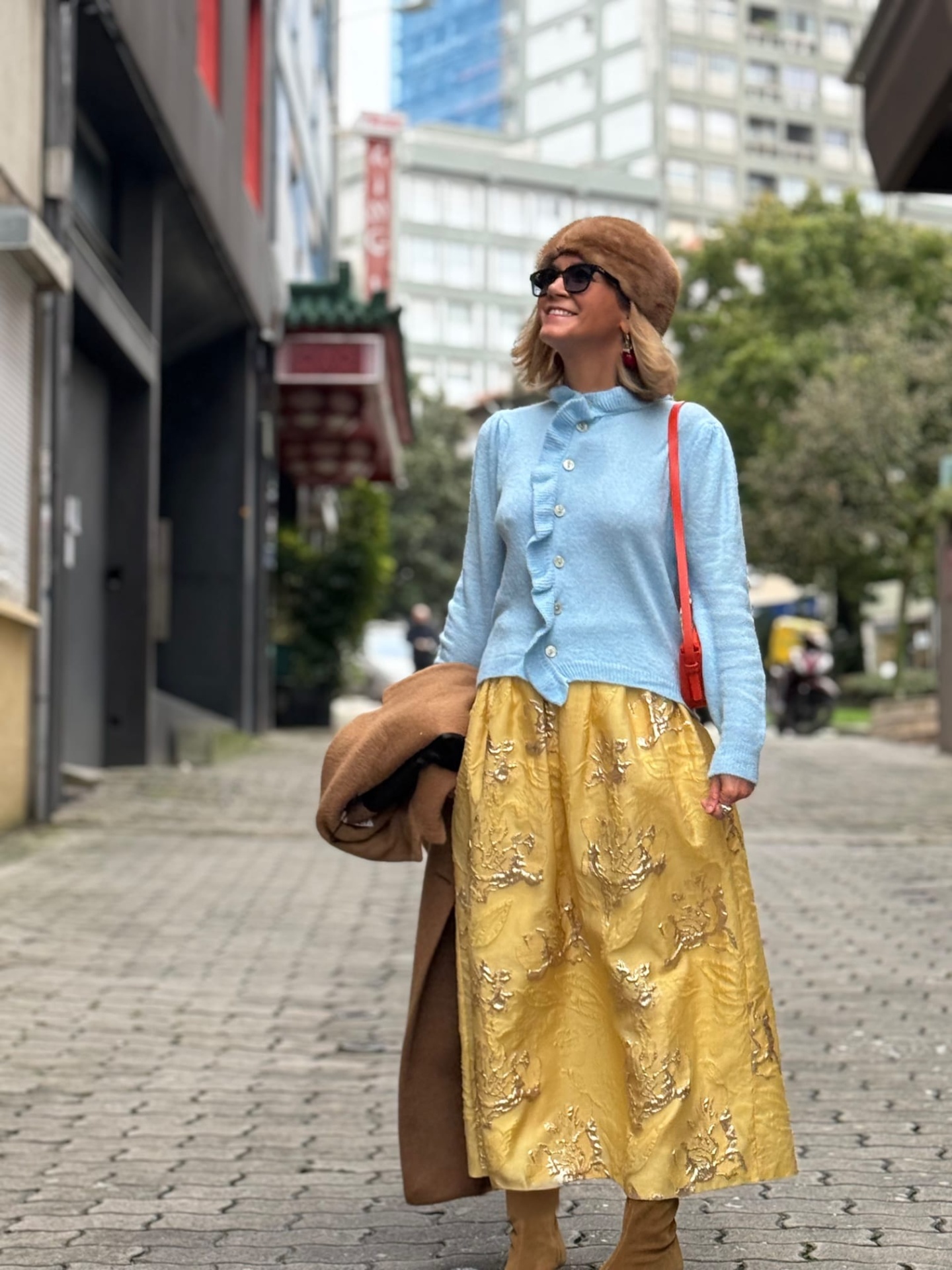 Mulher com roupa colorida numa rua pavimentada, com casaco, saia bordada e boina