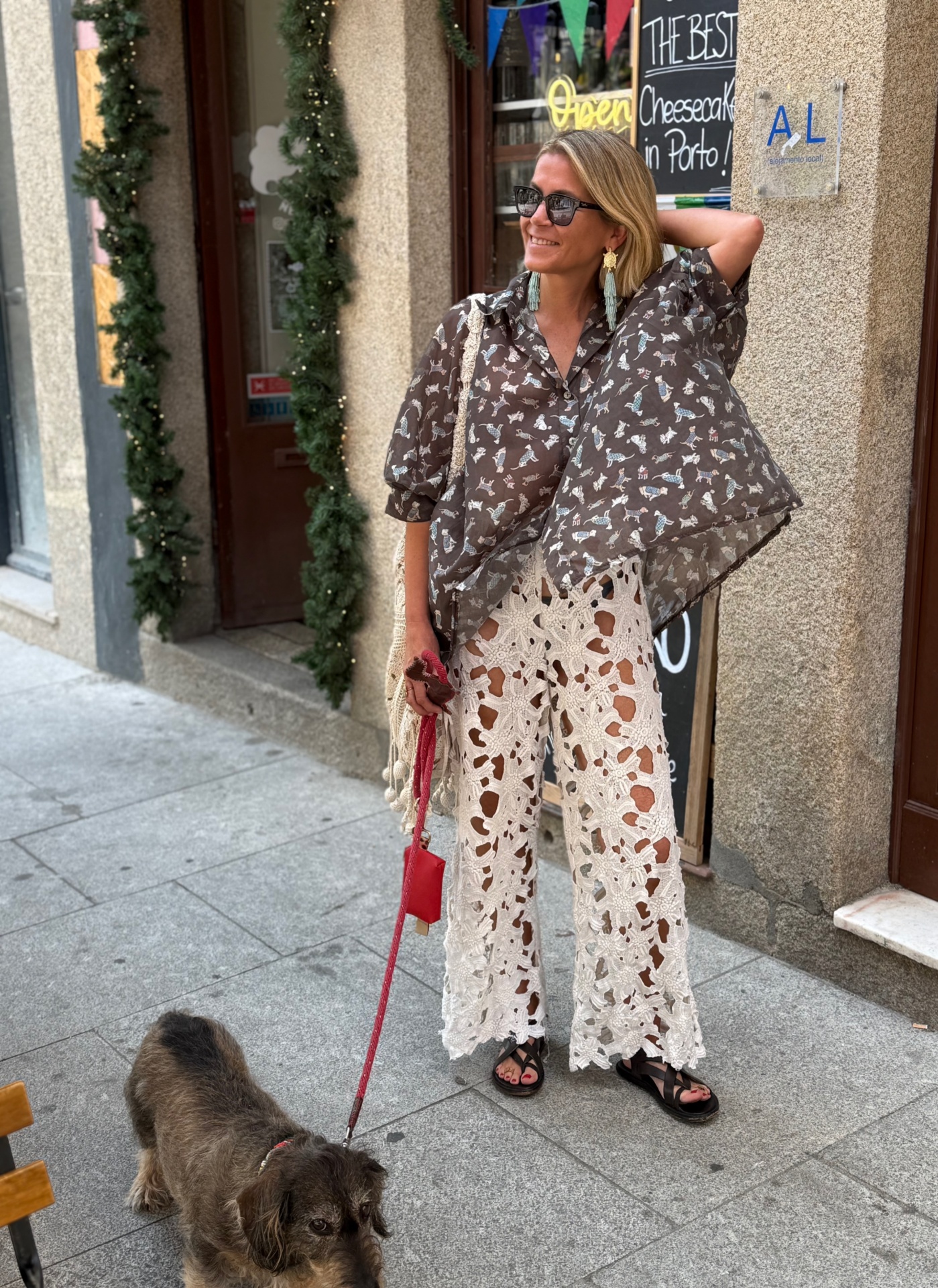 Mulher com camisa castanha com padrão de cães e calças brancas de crochet a passear cão castanho na rua