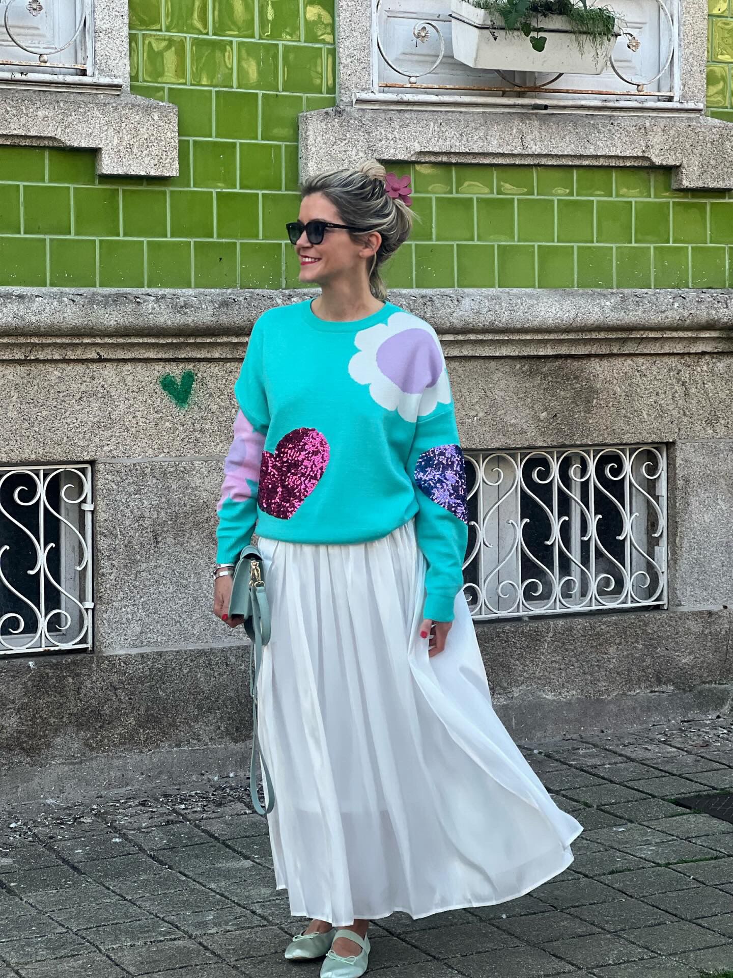 Mulher com camisola azul turquesa e saia longa branca em rua com azulejos verdes