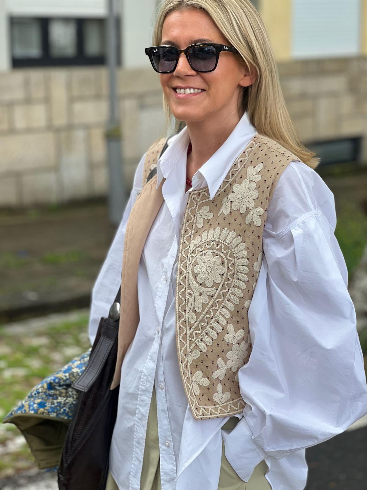 Colete bege bordado com camisa branca e óculos escuros preto ao ar livre