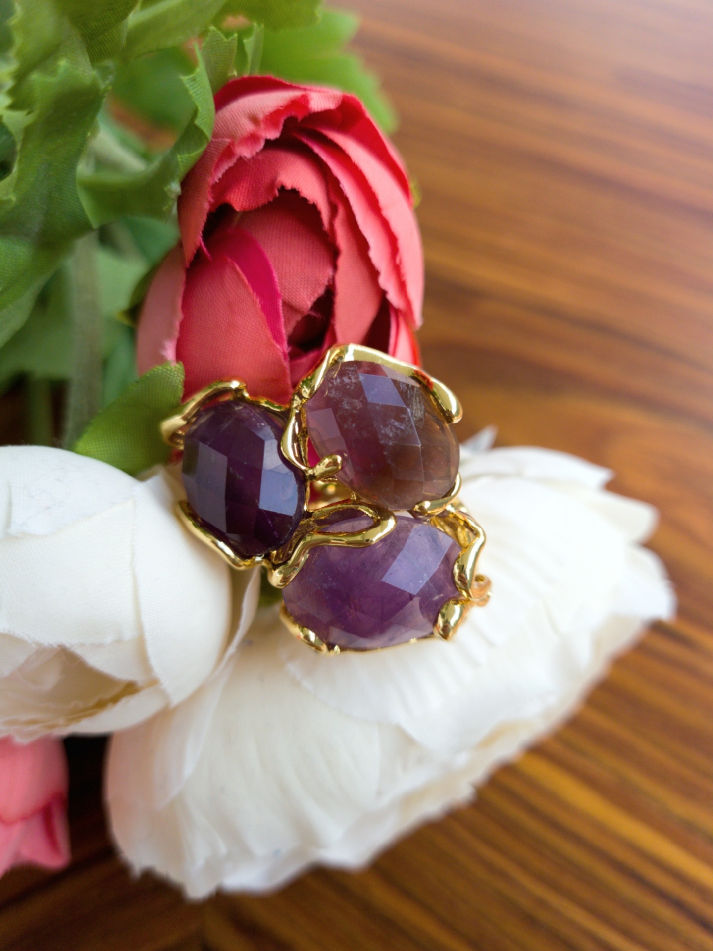 Anel dourado com pedras roxas sobre flores artificiais