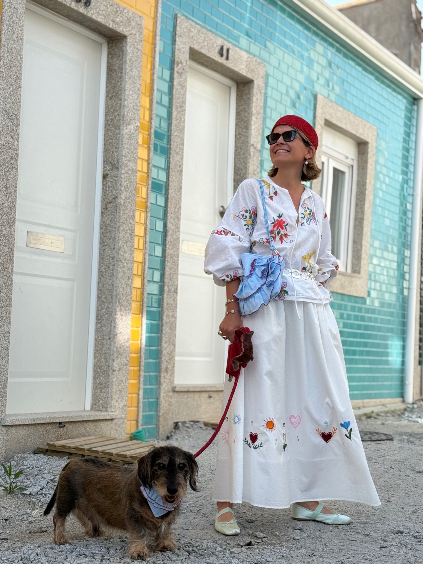 Mulher com vestido branco bordado e cão em rua com azulejos coloridos