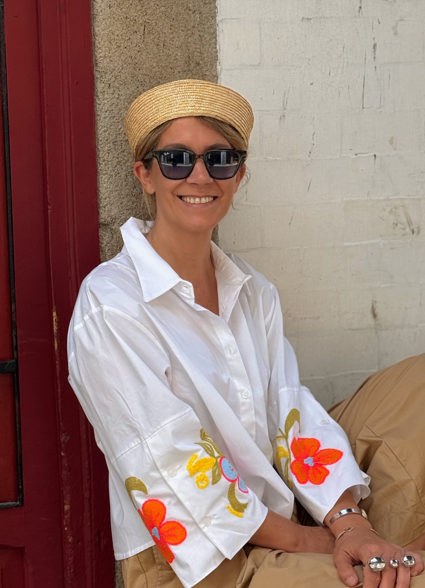 Mulher com camisa branca com flores bordadas, chapéu de palha e óculos escuros