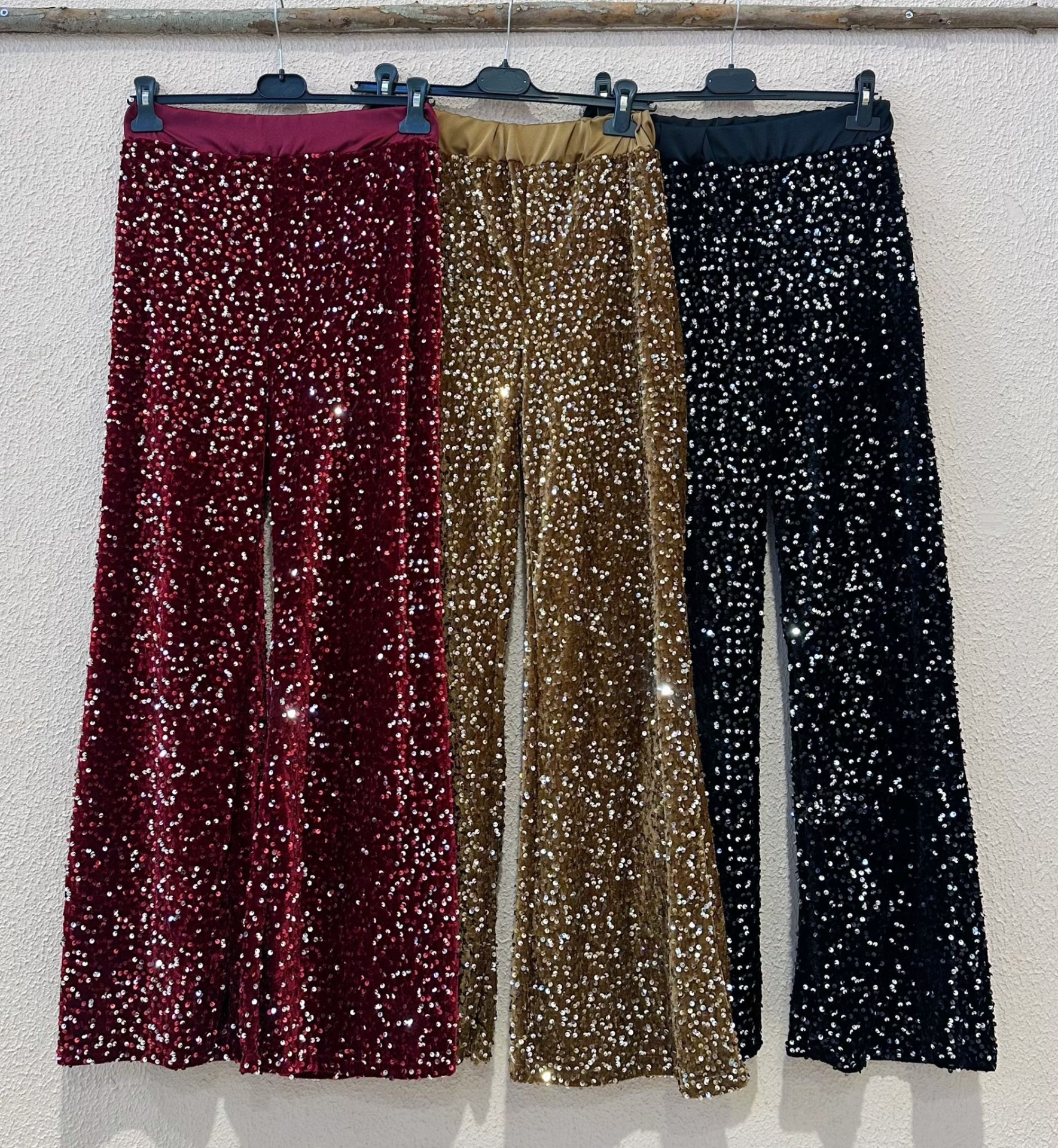 Três calças com lantejoulas em vermelho, dourado e preto penduradas
