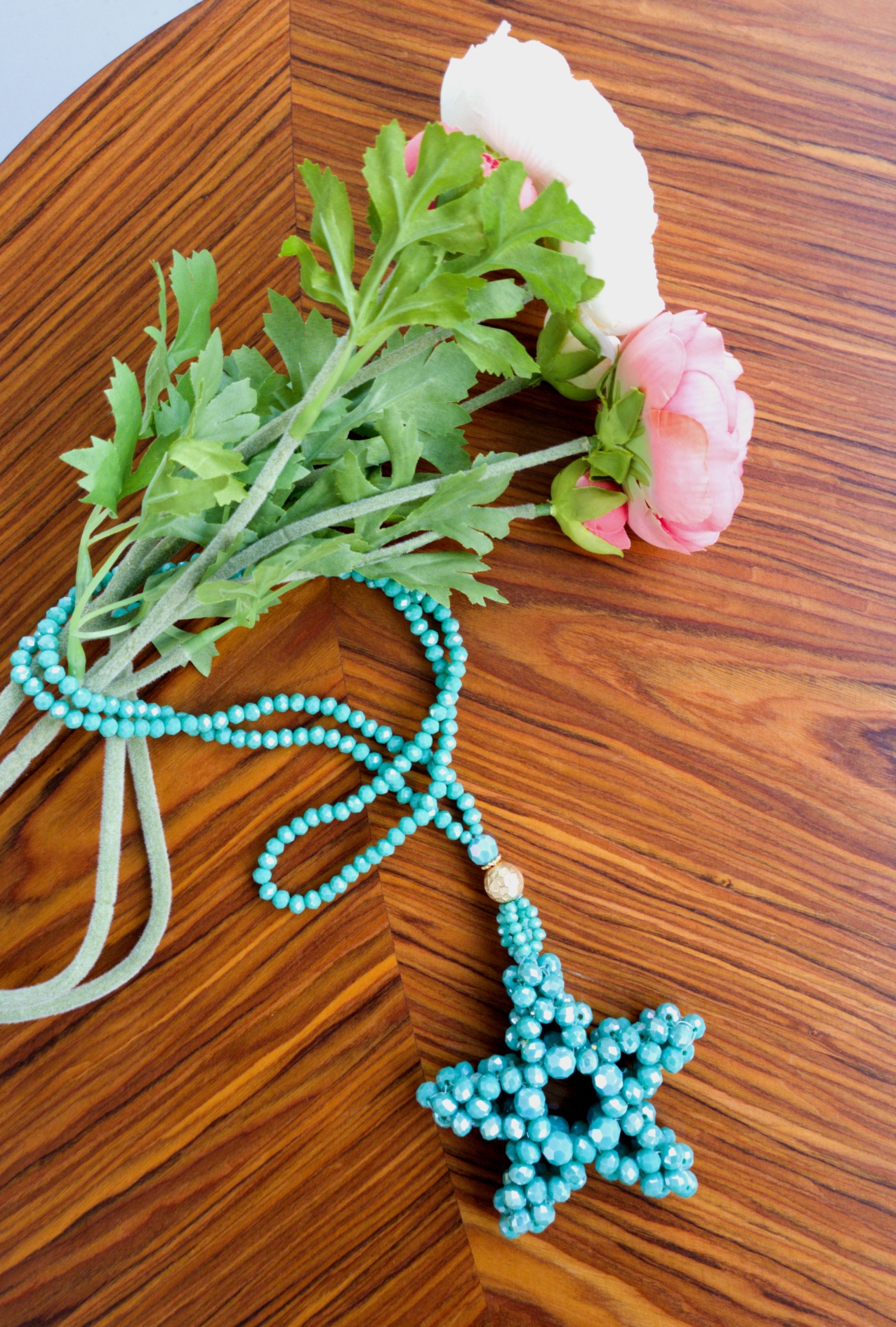 Colar azul claro em forma de estrela e flores sobre mesa de madeira