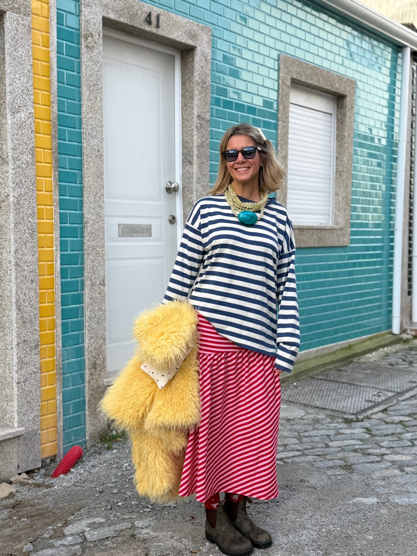 Mulher com roupa colorida e riscada numa rua com azulejos azuis no fundo