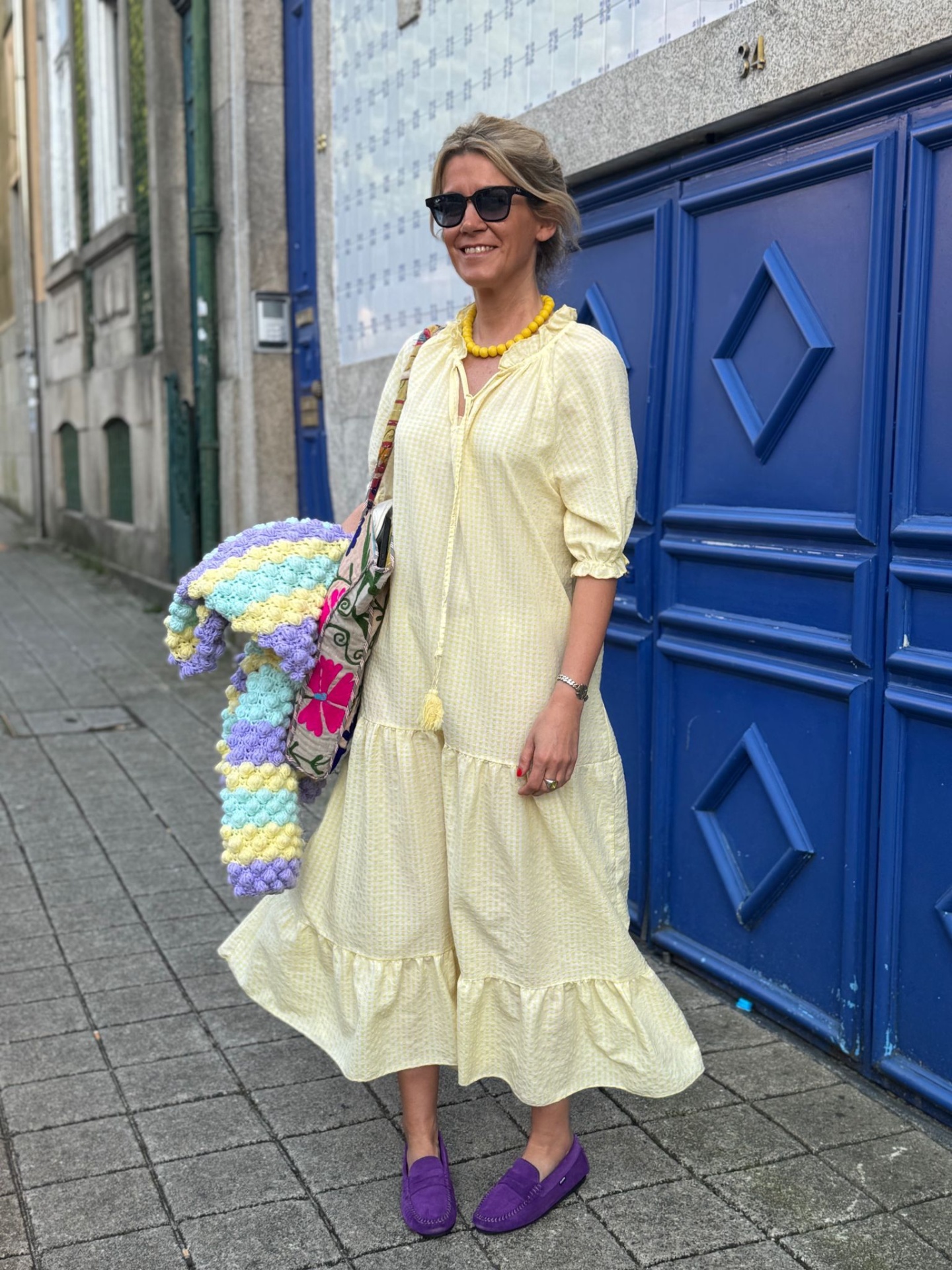 Mulher com vestido amarelo, sapatos roxos e manta tricot colorida em rua