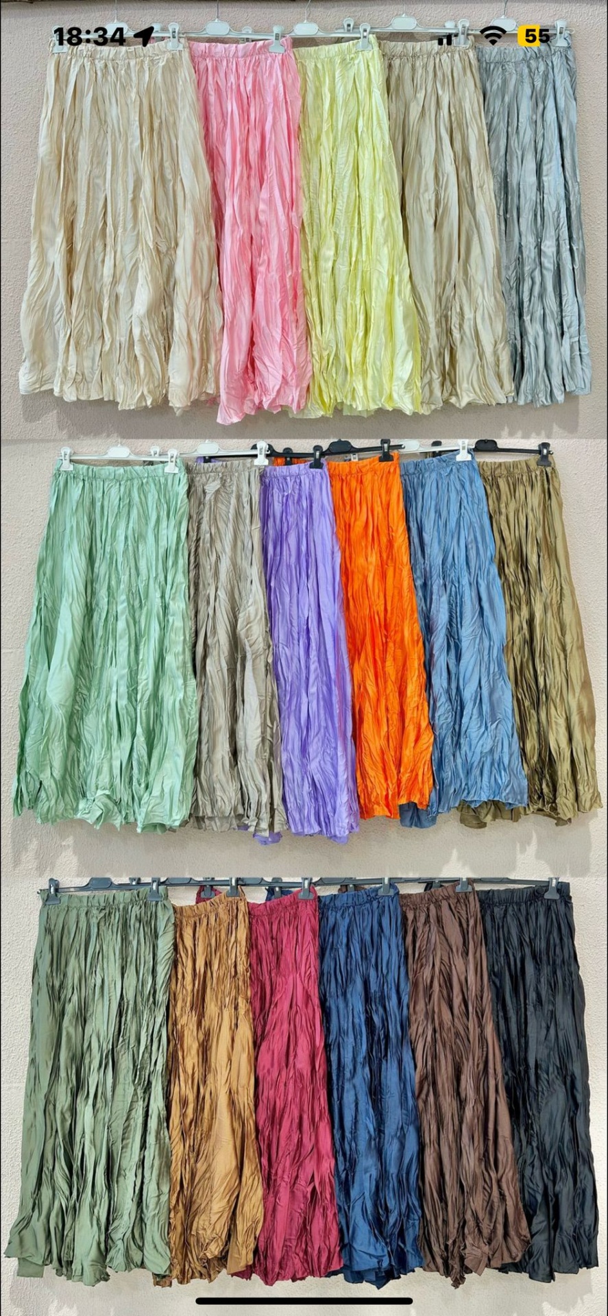 Três fileiras de saias longas franzidas em várias cores penduradas numa parede clara.