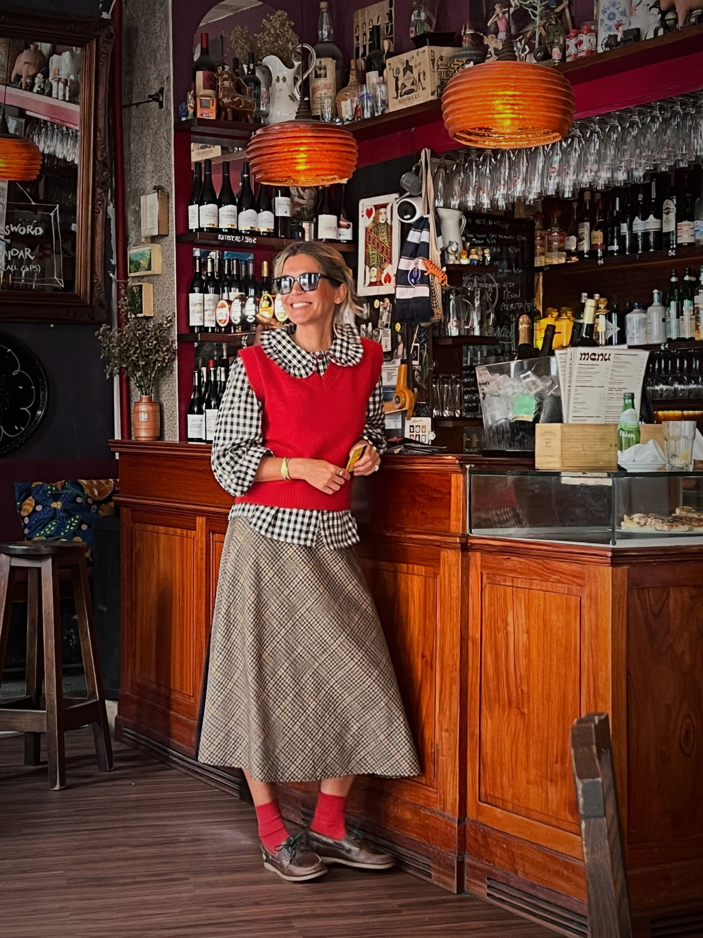 Mulher com blusa xadrez e colete vermelho em cafetaria com barril de vinho