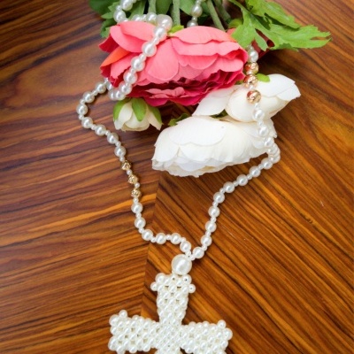 Colar de pérolas com crucifixo em forma de cruz e flores artificiais sobre mesa de madeira