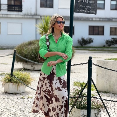 Mulher com camisa verde e saia estampada em rua com prédio ao fundo