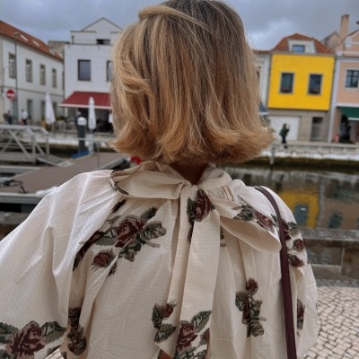 Blusa branca com padrão floral e gravata no pescoço vista de trás