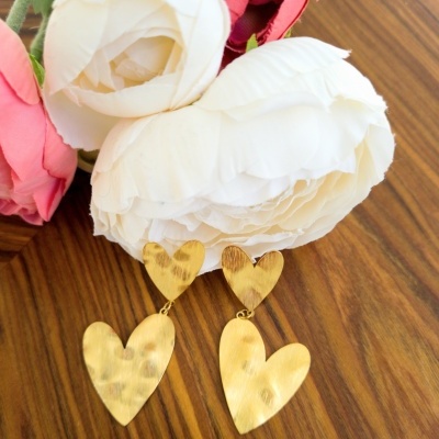 Brincos dourados em forma de coração com flores artificiais ao lado.