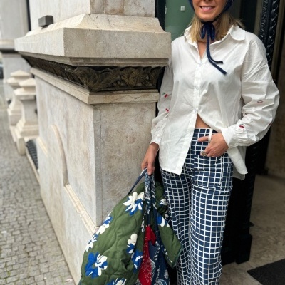 Mulher com roupa casual e bolsa acolchoada floral numa rua com calçada de pedra.
