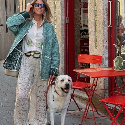 Mulher com casaco verde e calças rendadas na rua com cão branco ao lado