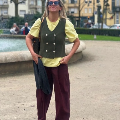 Mulher com colete verde-oliva, t-shirt amarela, calças vinho e ténis vermelhos num parque