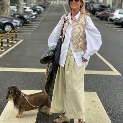 Mulher com roupa clara e colete bege com cão numa passadeira na rua