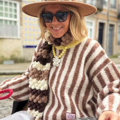 Mulher com casaco riscado, echarpe castanha, chapéu castanho e óculos escuros a beber chá