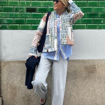 Pessoa com casaco patchwork colorido e óculos em frente a parede de azulejos verdes