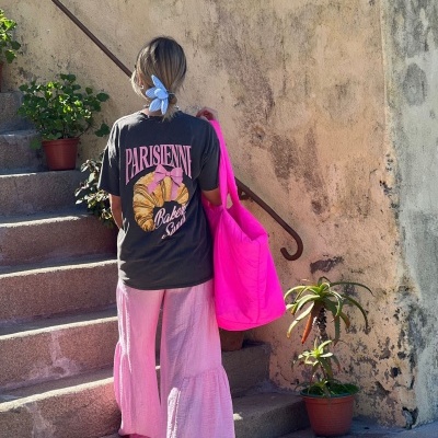 Pessoa de costas com roupa casual e bolsa rosa subindo escadas externas com parede envelhecida e plantas.