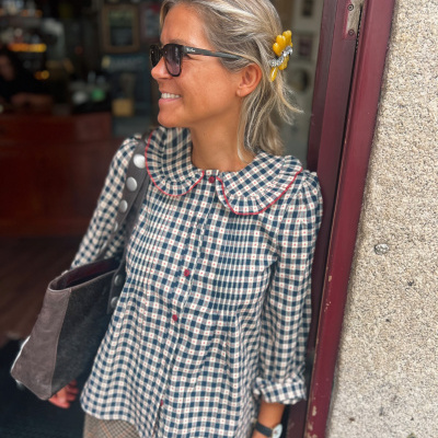 Blusa quadriculada azul e creme com botões vermelhos e gola arredondada, mola de cabelo amarela, mulher com óculos de sol pretos