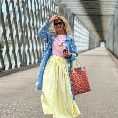 Mulher com casaco azul, saia amarela e t-shirt rosa em passadeira metálica