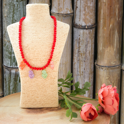 Colar vermelho com pendentes de coruja em busto creme com flores cor de rosa e bambus ao fundo