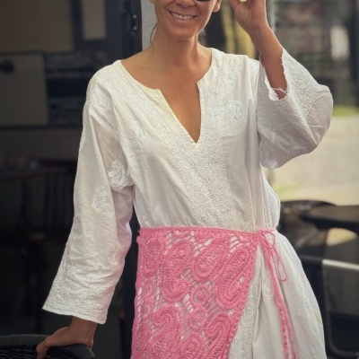 Vestido branco bordado, cinto rosa croché, óculos de sol pretos, lenço cabeça branco com padrão colorido.