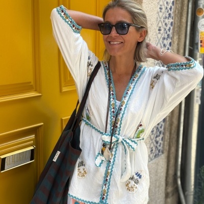 Mulher com blusa branca bordada, calças brancas e óculos de sol pretos