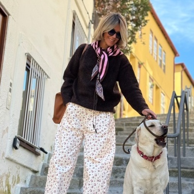 Mulher com calças largas brancas com padrão floral e casaco preto com cão Labrador branco numa escadaria